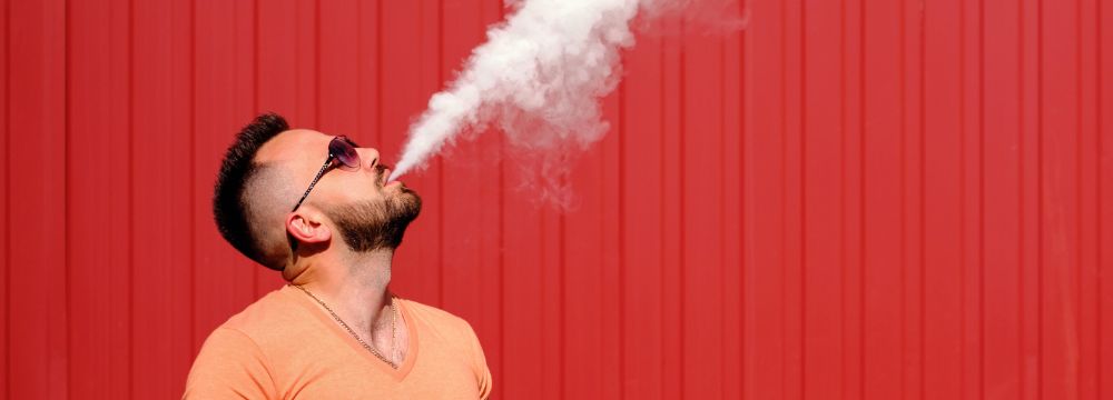 Man exhales vapor form his e-cigarette wrongly believing is it less damaging than a cigarette 