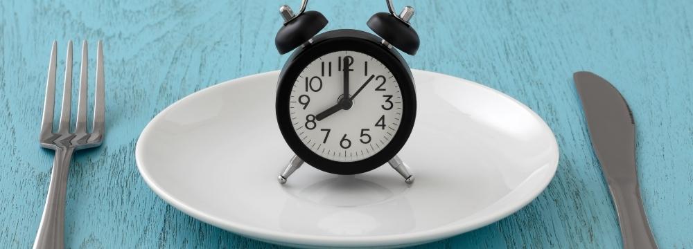 plate with alarm clock on it, in between fork and knife