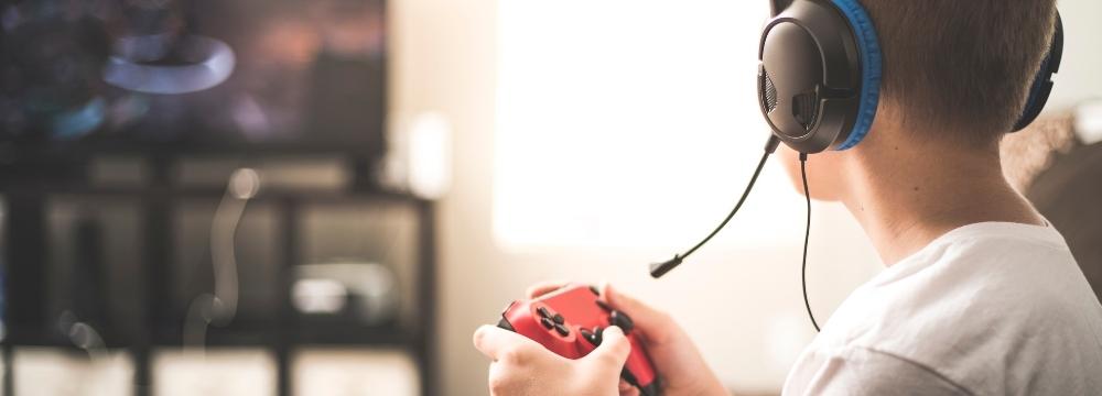 young boy with headset holding a controller playing his video game on the tv