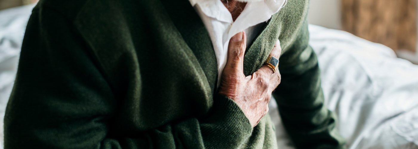 Older man sitting up in bed gripping chest with hand 