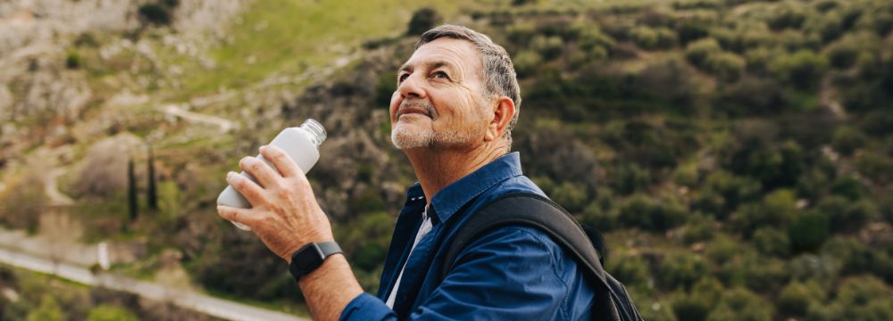 Man in mountains drinking from water bottle in hiking gear 